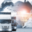Quatro caminhões à frente de um globo terrestre representam a transformação digital na logística.