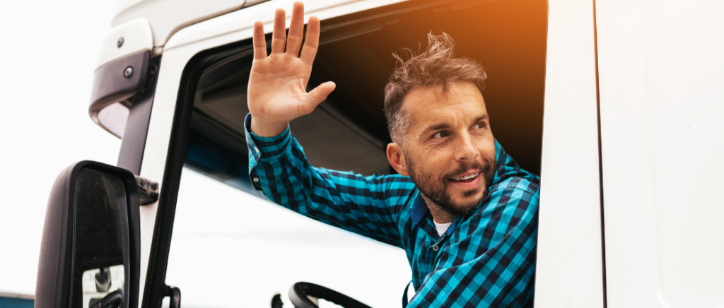 Motorista dentro de caminhão acenando, ilustra a atualização da Tabela de frete ANTT 2024.