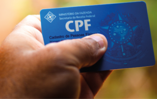 A imagem mostra a mão de uma pessoa segurando um documento. Ela está com o CPF nas mãos, representando uma pessoa que se preocupa com a segurança dos seus documentos ao fazer um cadastro.
