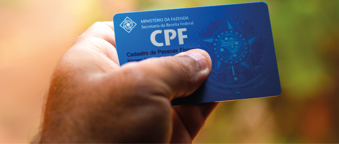 A imagem mostra a mão de uma pessoa segurando um documento. Ela está com o CPF nas mãos, representando uma pessoa que se preocupa com a segurança dos seus documentos ao fazer um cadastro.