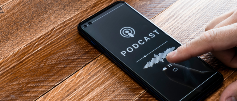 Pessoa tocando a tela de um smartphone com um podcast aberto, pronta para reproduzir o áudio, num ambiente com fundo de madeira.