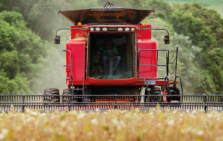 Uma máquina está colhendo itens em uma plantação. A imagem representa o volume de fretes do agronegócio.