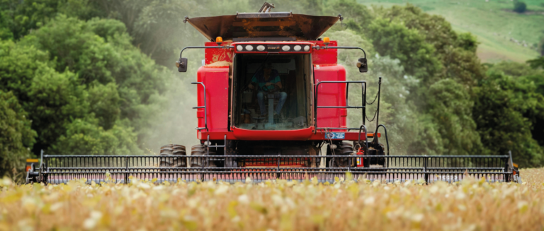 Uma máquina está colhendo itens em uma plantação. A imagem representa o volume de fretes do agronegócio.