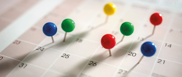 Um calendário está com vários pins coloridos sobre ele, representando marcações de imprevistos e oportunidades que uma transportadora precisa lidar.