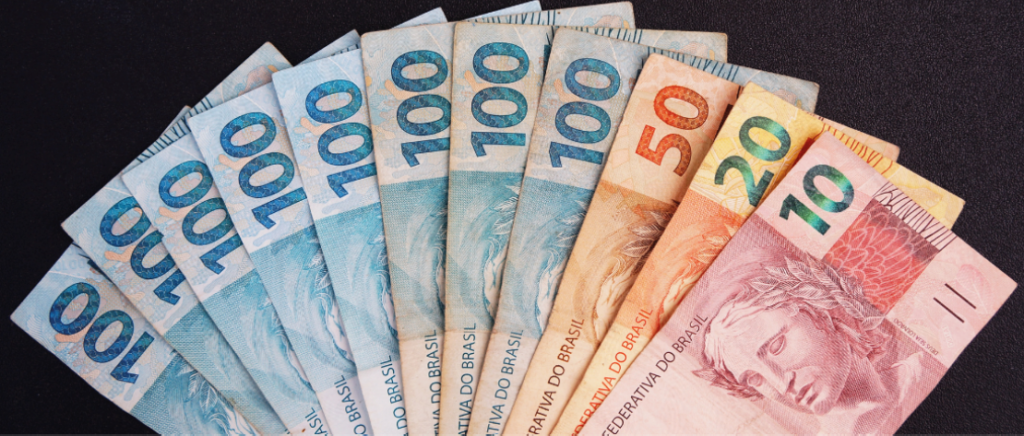 A imagem mostra várias notas sobre um fundo preto, representando o crédito para as transportadoras. Tem uma nota de R$10, uma de R$20, uma de R$50 e oito de R$100, totalizando a quantia de R$880.
