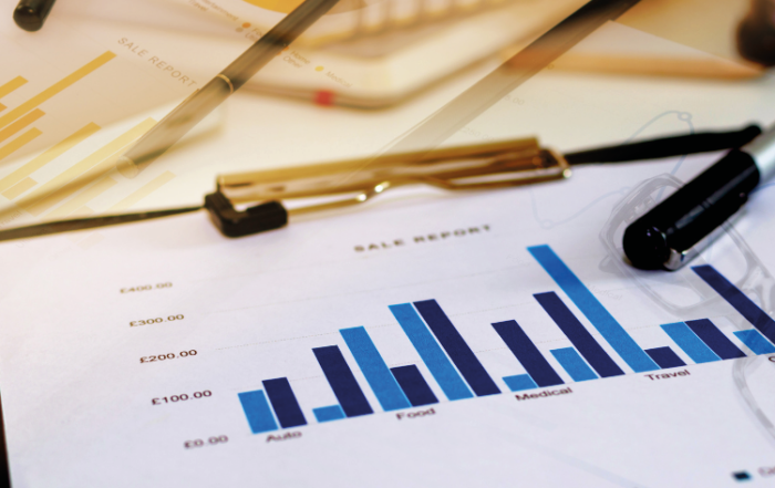 A imagem mostra uma mesa com um relatório de vendas em uma prancheta, representando os indicadores financeiros de uma transportadora em crescimento.