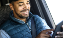 A imagem mostra um motorista dentro de seu caminhão. Ele está sentado no banco, usando o cinto de segurança e o veículo está parado. O motorista está mexendo em um tablet, representando a avaliação da empresa dentro da plataforma da Fretebras.