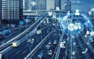A imagem mostra, em segundo plano, várias pistas em uma cidade grande com diversos veículos circulando ao mesmo tempo, inclusive caminhões. Em primeiro plano, vários símbolos estão sobrepostos, como o sinal de wi-fi, e-mail, telefone, aparelho de celular etc., representando as tecnologias para a segurança do transporte rodoviário de cargas.