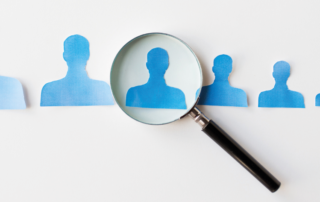 A imagem mostra o perfil de 7 bonecos na cor azul. O tamanho deles começa maior ao lado esquerdo e vai diminuindo conforme se aproxima do lado direito. Uma lupa está sobre o terceiro desenho, representando os riscos na hora da contratação dos motoristas.