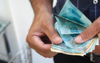A imagem mostra uma pessoa contando dinheiro. Ela está com várias notas de R$50 e R$100 nas mãos, representando o motorista que pediu o saldo antecipado.
