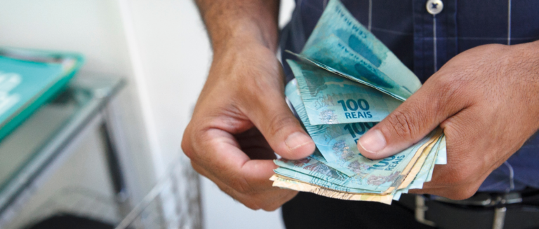 A imagem mostra uma pessoa contando dinheiro. Ela está com várias notas de R$50 e R$100 nas mãos, representando o motorista que pediu o saldo antecipado.