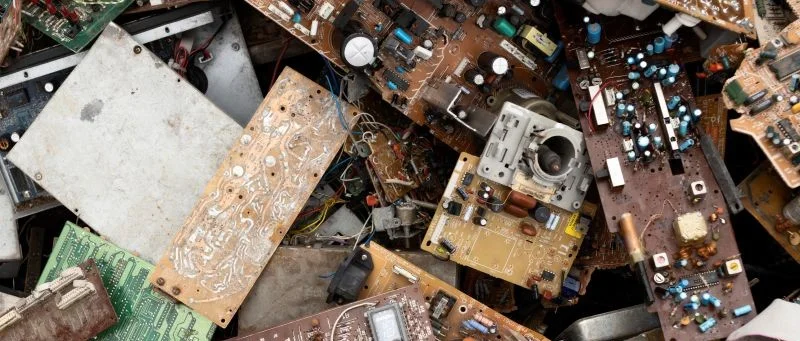 Uma pilha de placas de circuito e componentes eletrônicos descartados e empoeirados, representando o acúmulo de lixo eletrônico que precisa ser gerenciado e reciclado através de um sistema eficiente de logística reversa.