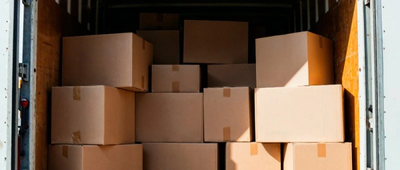 Vista do interior de um baú de caminhão aberto, repleto de caixas de papelão de diferentes tamanhos empilhadas, ilustrando a otimização de espaço e a consolidação de mercadorias no transporte de carga fracionada.
