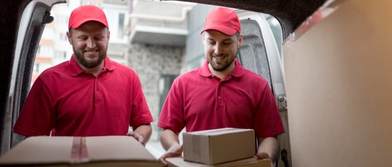 Dois entregadores segurando caixas de papelão em um veículo de carga, representando o a distribuição logística de empresas que utilizam o modelo de agregados.